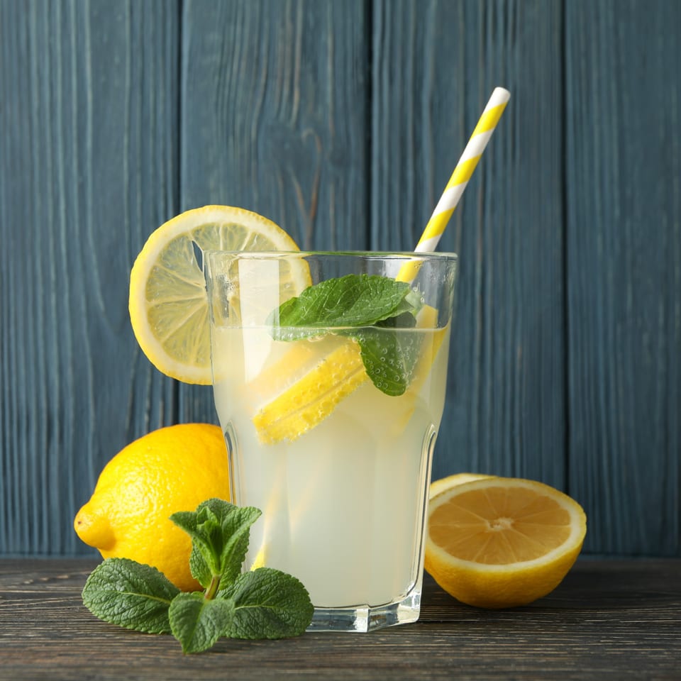 Refreshing lemonade with lemon slices, mint, and a striped straw, surrounded by fresh lemons.