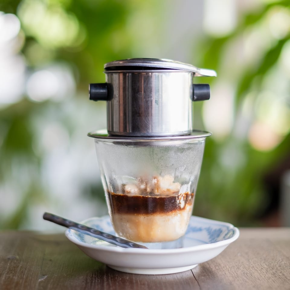 Vietnamese coffee brewing in a phin filter over a glass with condensed milk on a wooden table.