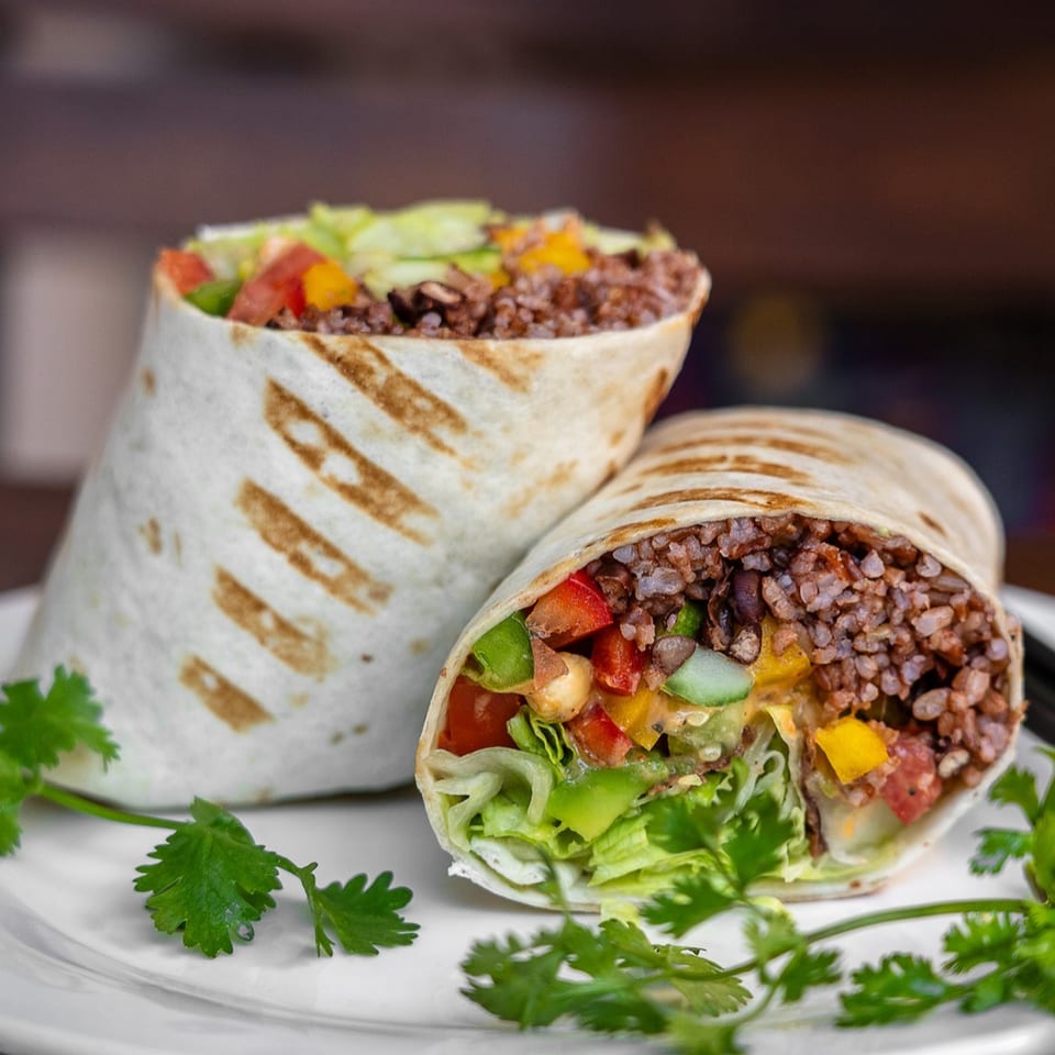 Two PX JAVA burritos filled with rice, beans, lettuce, tomatoes, and peppers, garnished with cilantro.